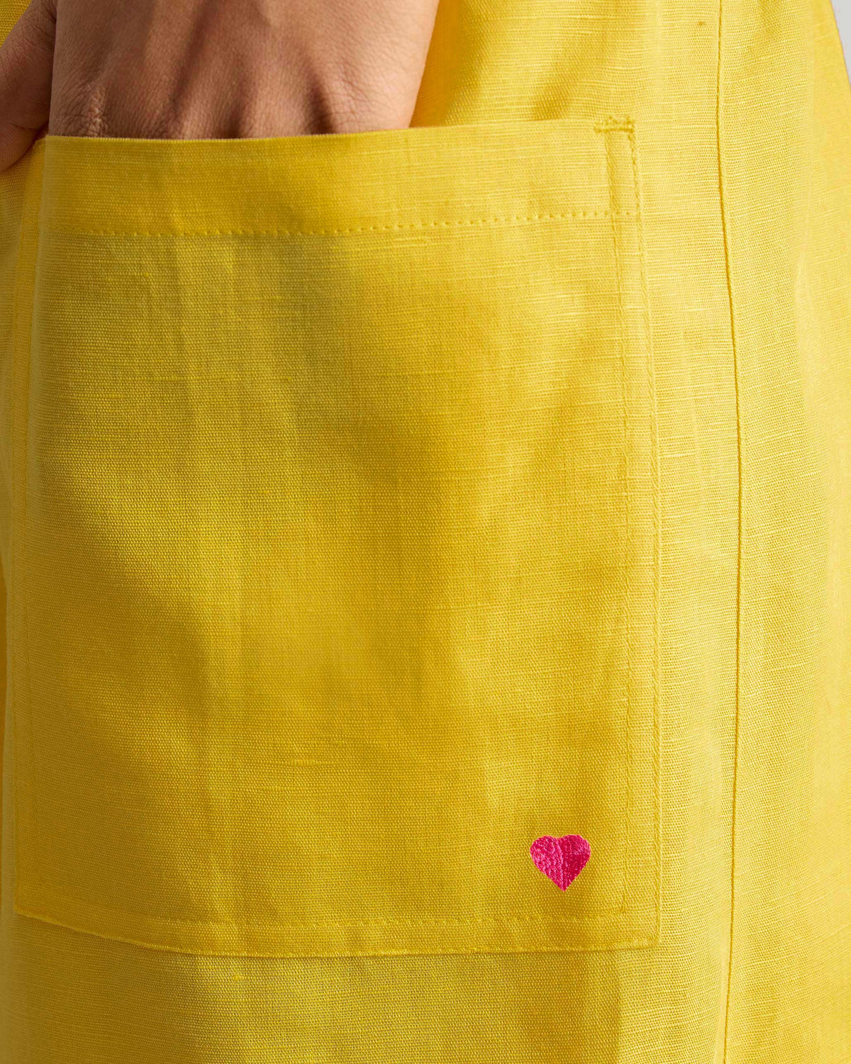 Close-up of yellow Serene pants with a pink embroidered heart on the patch pocket.