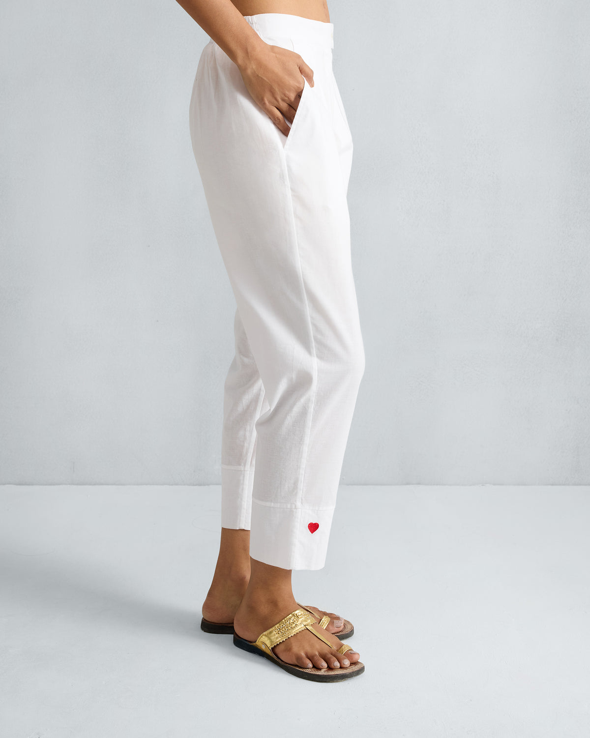 Side view of white Narrow pants with a red heart at the cropped hem.