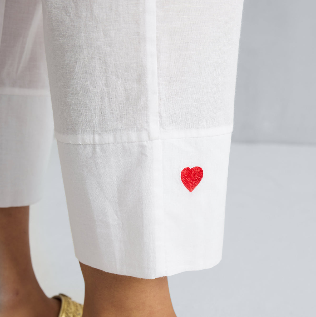 Close-up of a red embroidered heart on the cuff of white Narrow pants.