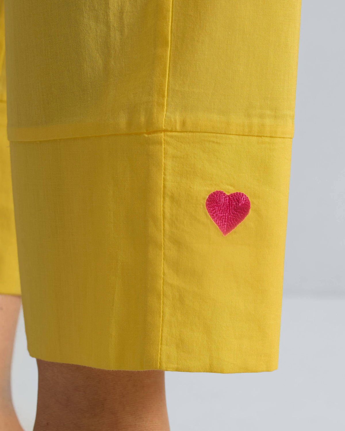 Close-up of a red heart embroidered on the hem of yellow Narrow pants.
