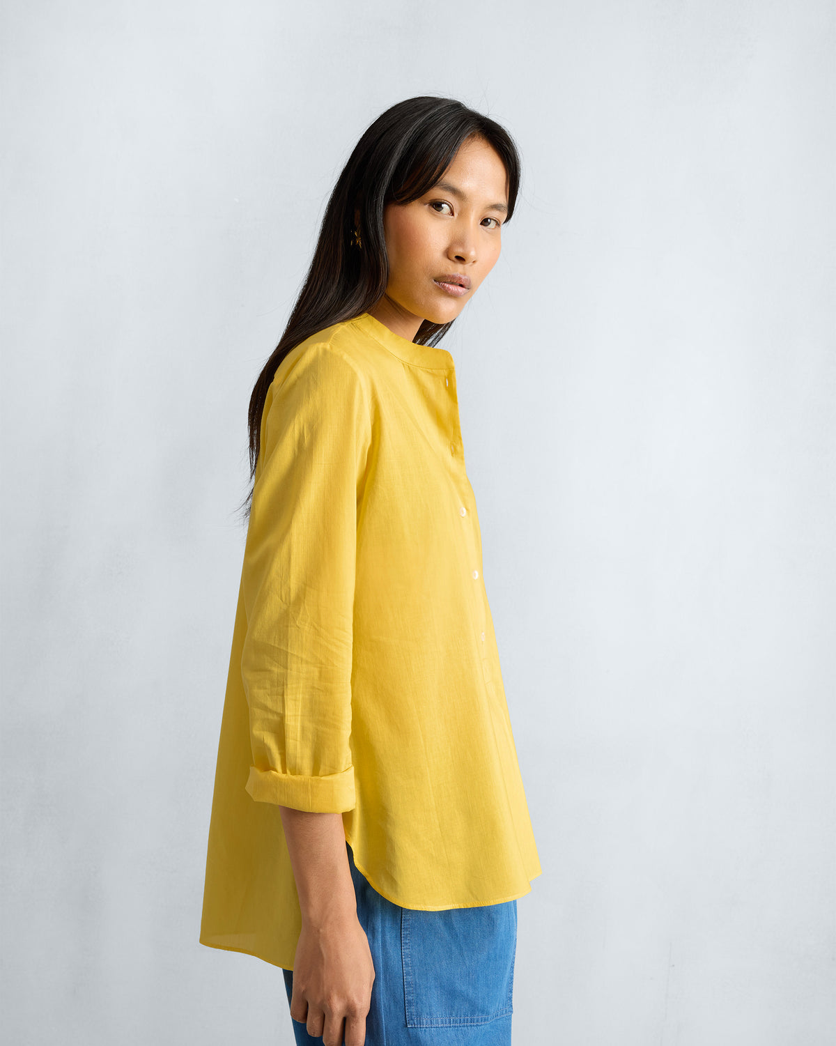 Side view of a yellow mandarin collar top with a curved hem.