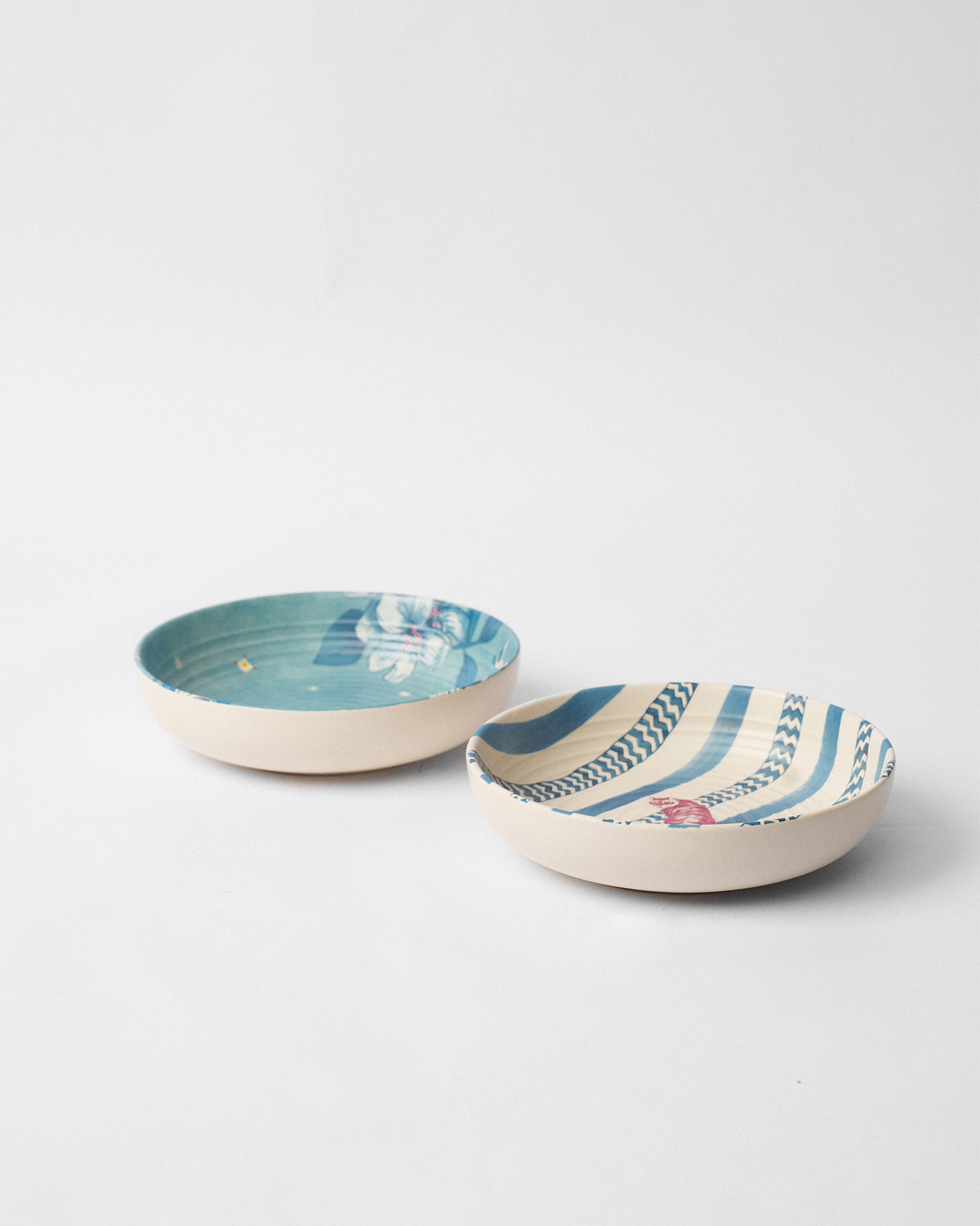 Pair of River Tiger shallow bowls with teal floral and blue striped interiors.