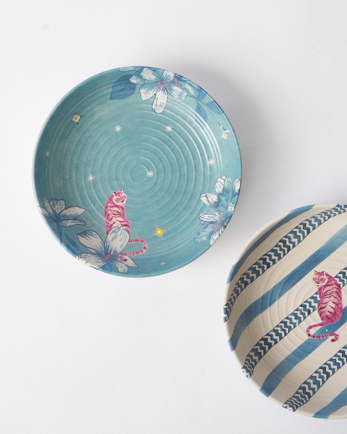 River Tiger shallow bowls from above showing pink tigers on teal floral and blue striped grounds.