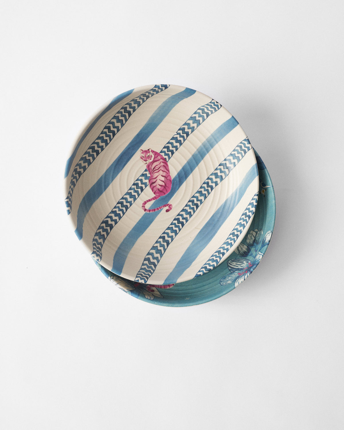Stacked River Tiger shallow bowls with a pink tiger on blue stripes over a teal floral bowl.