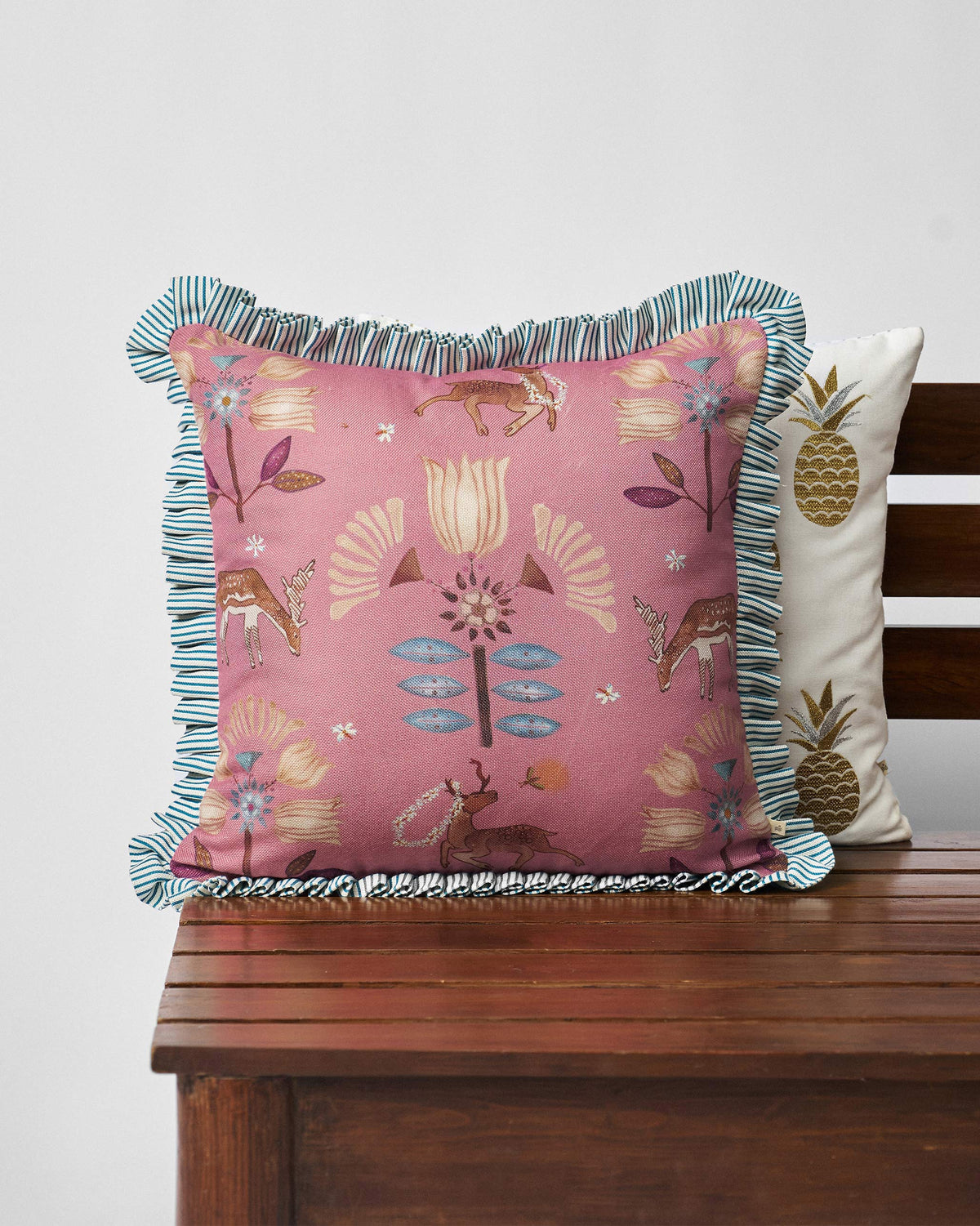 Deer Dance Cushion in pink with deer and flower motifs and a striped frill edge.
