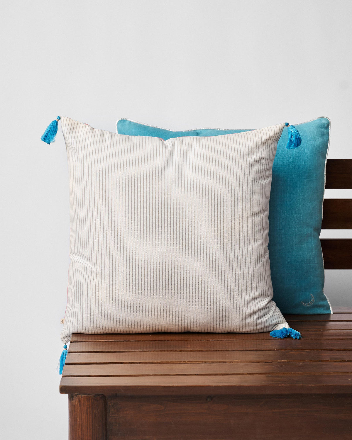 Cream pinstripe cushion cover with blue tassels.