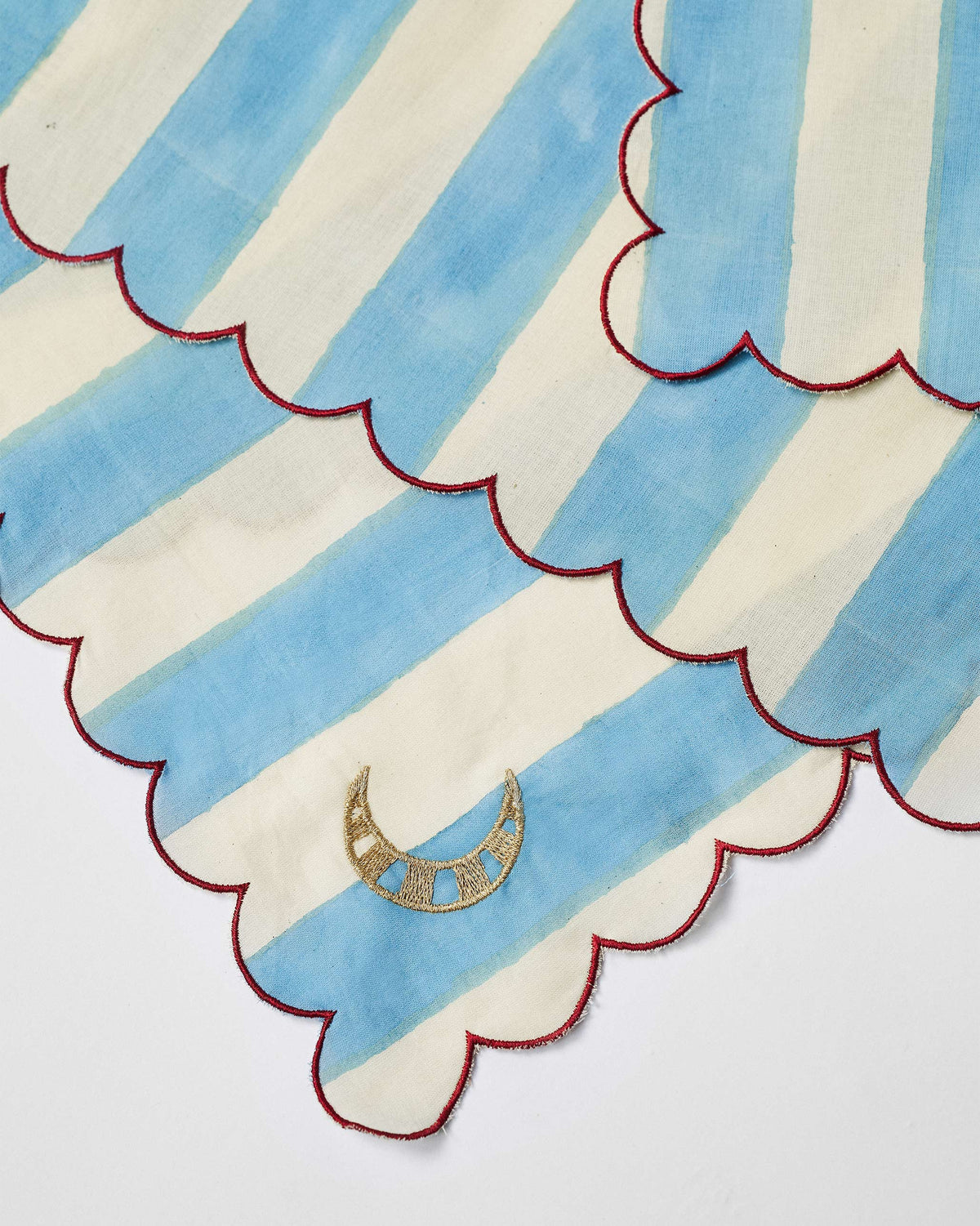 Close-up of a river-stripe napkin with a red scalloped edge and gold moon.