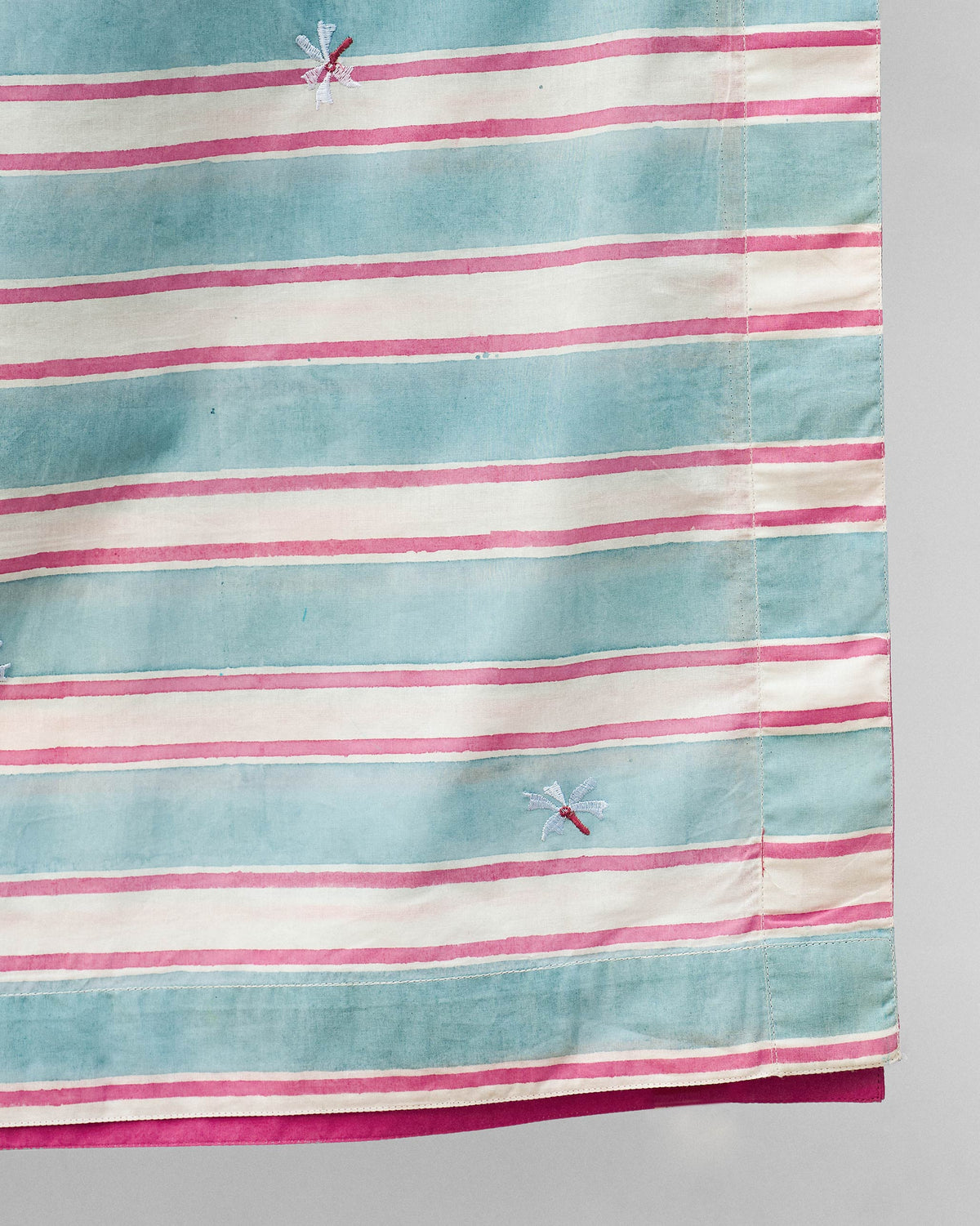 Close-up of Parijat table cover showing blue and pink stripes and small embroidered motifs.