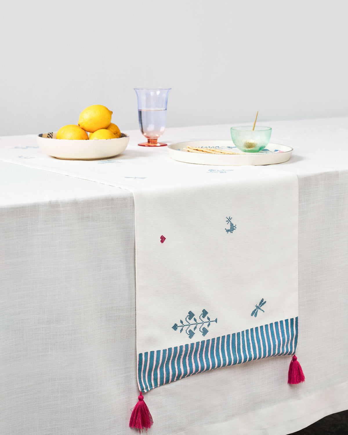 Mayur table runner laid on a table with teal motifs and tassels.