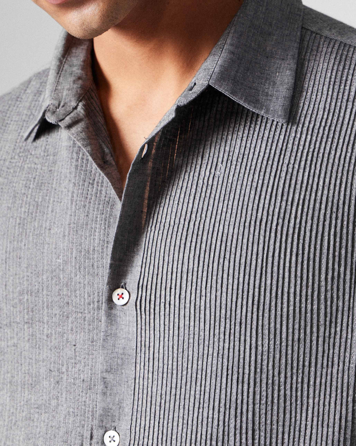 Close-up of a charcoal Nava shirt showing pintucks and white buttons with red stitching.