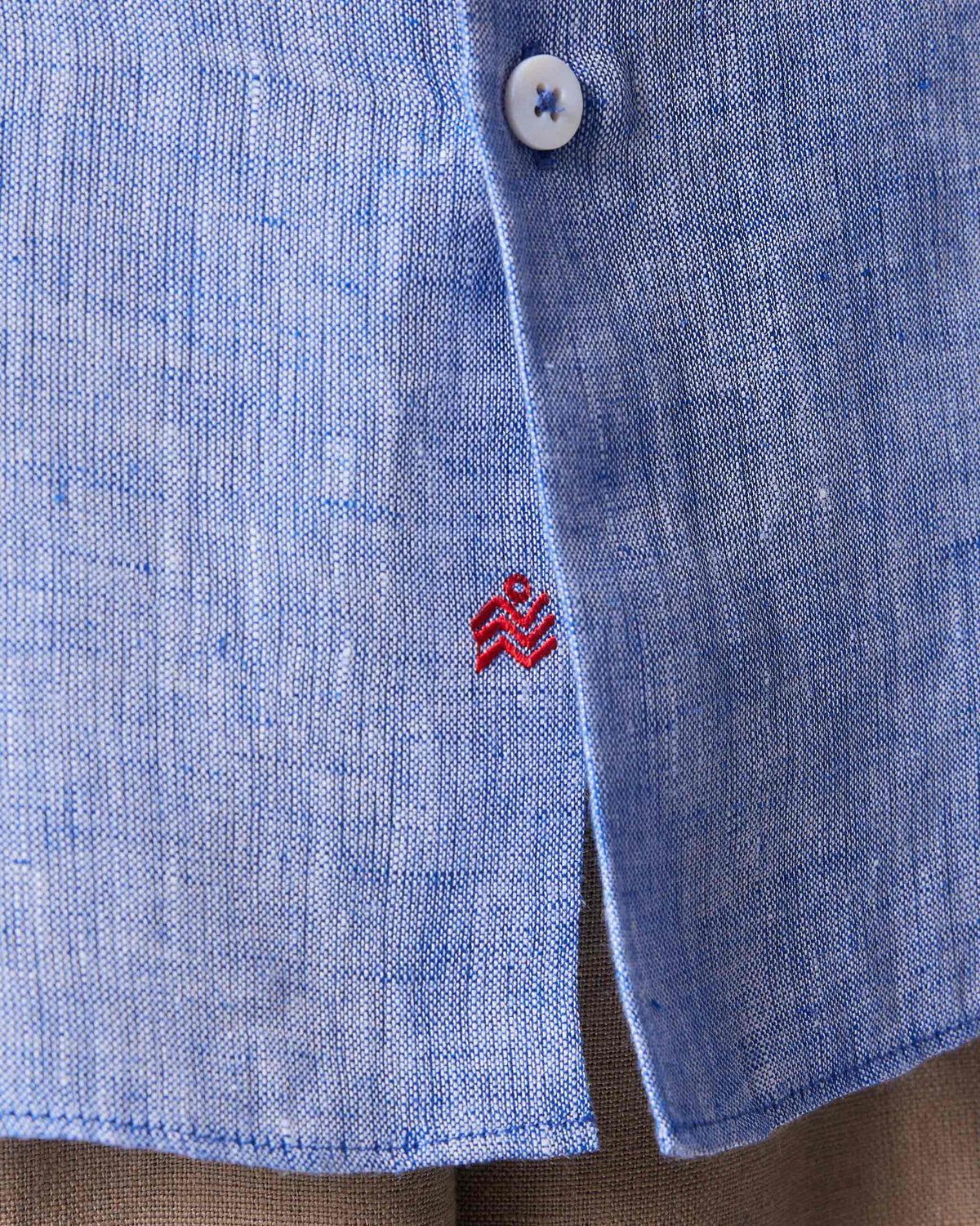 Close-up of a light blue Hakuna Shirt showing a red logo at the placket hem.