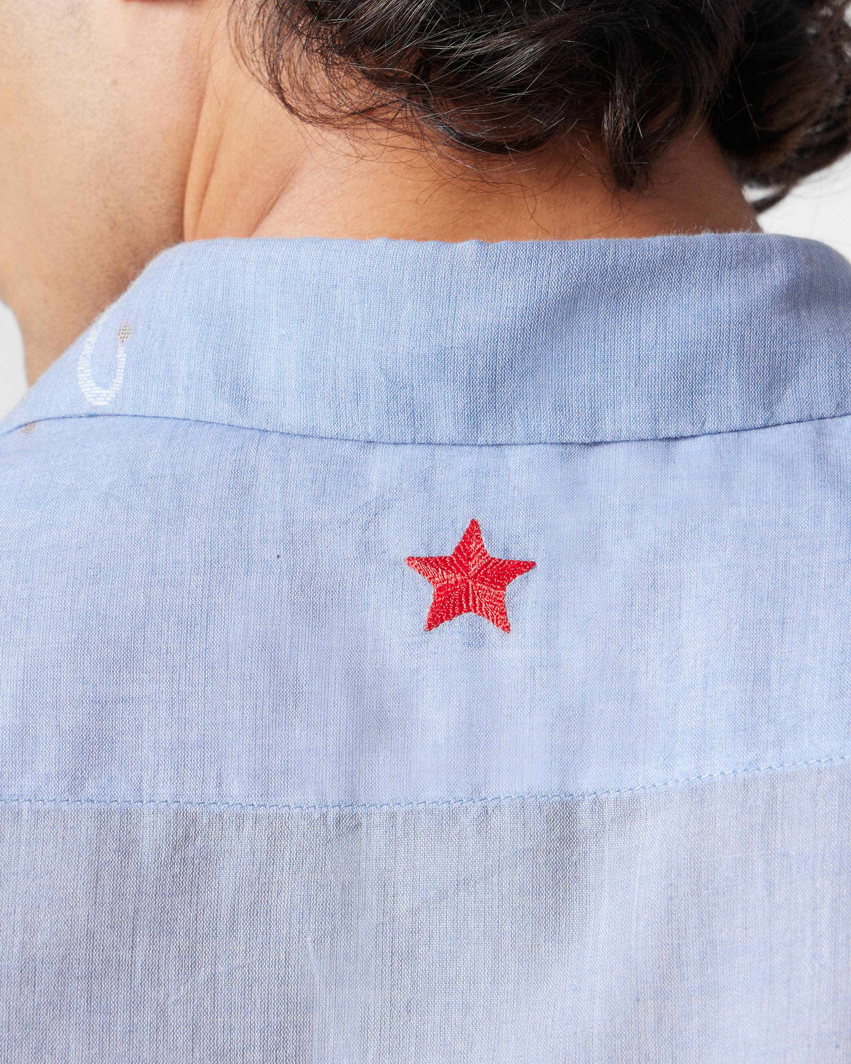 Close-up of a red star on the back yoke of a light blue half-sleeve shirt.