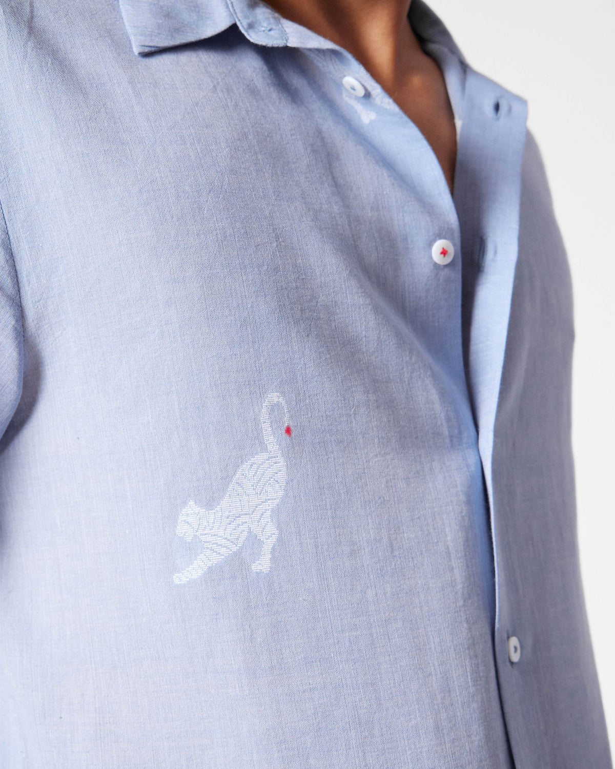 Close-up of white animal embroidery on a light blue half-sleeve shirt.