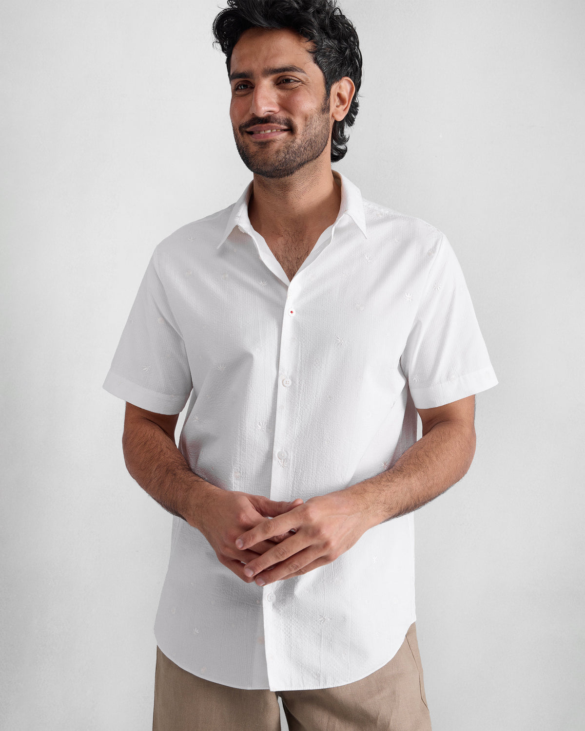 Person wearing a white half sleeve shirt with scattered tonal embroidery.