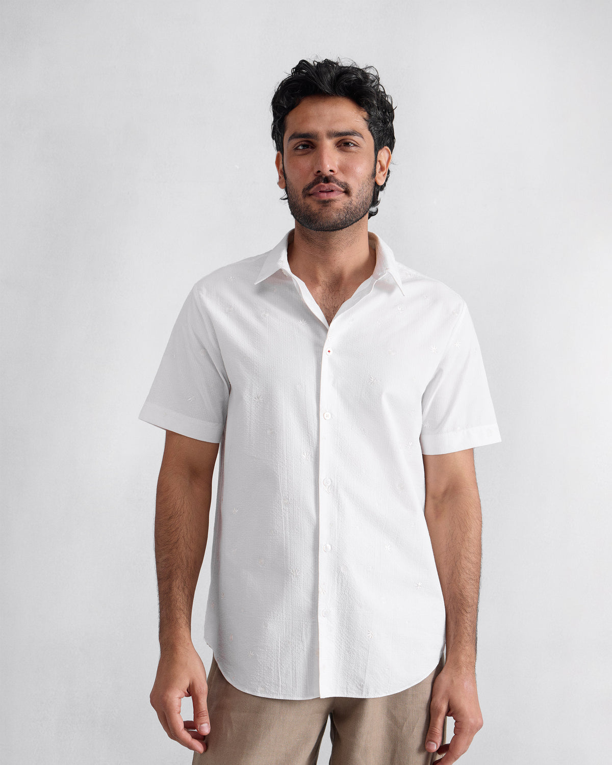 Person wearing a white embroidered half sleeve shirt with an open collar.