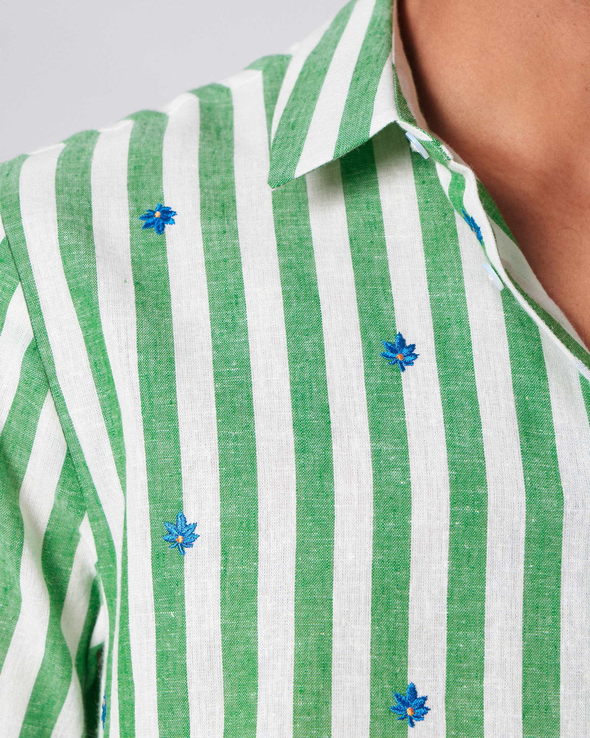 Close-up of blue leaf embroidery on a green-and-white striped half-sleeve shirt.