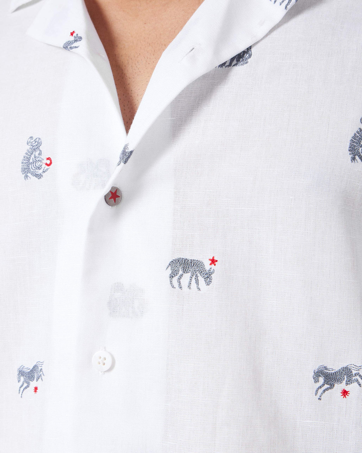 Close-up of a white Mistari Shirt showing navy animal embroidery and a red star button.
