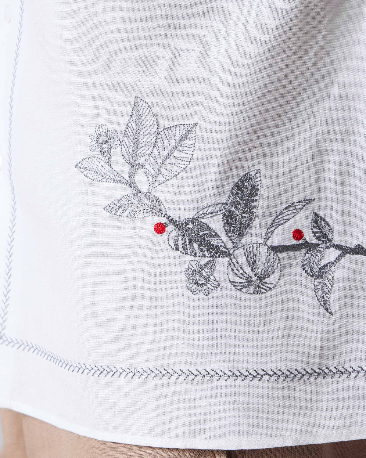 Close-up of floral embroidery with red berries near the hem of a white Delta shirt.