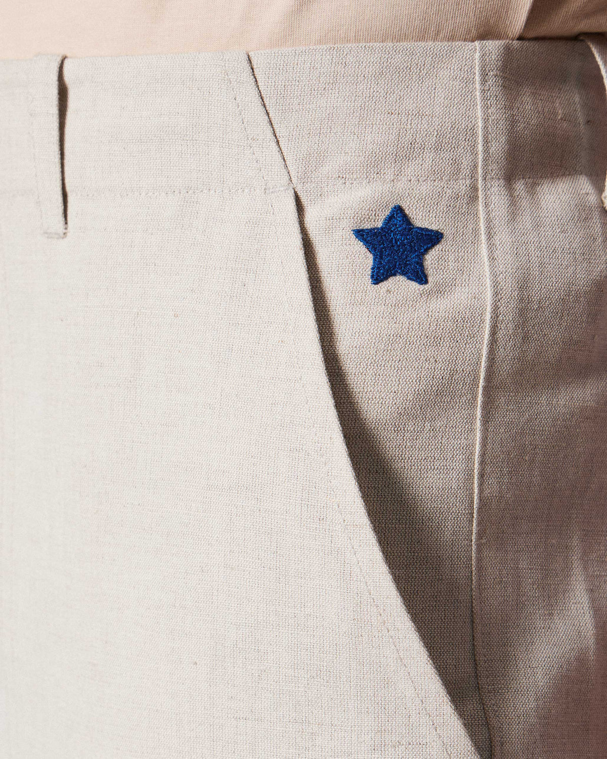 Close-up of ivory Zar Pants with a blue star embroidered at the pocket.