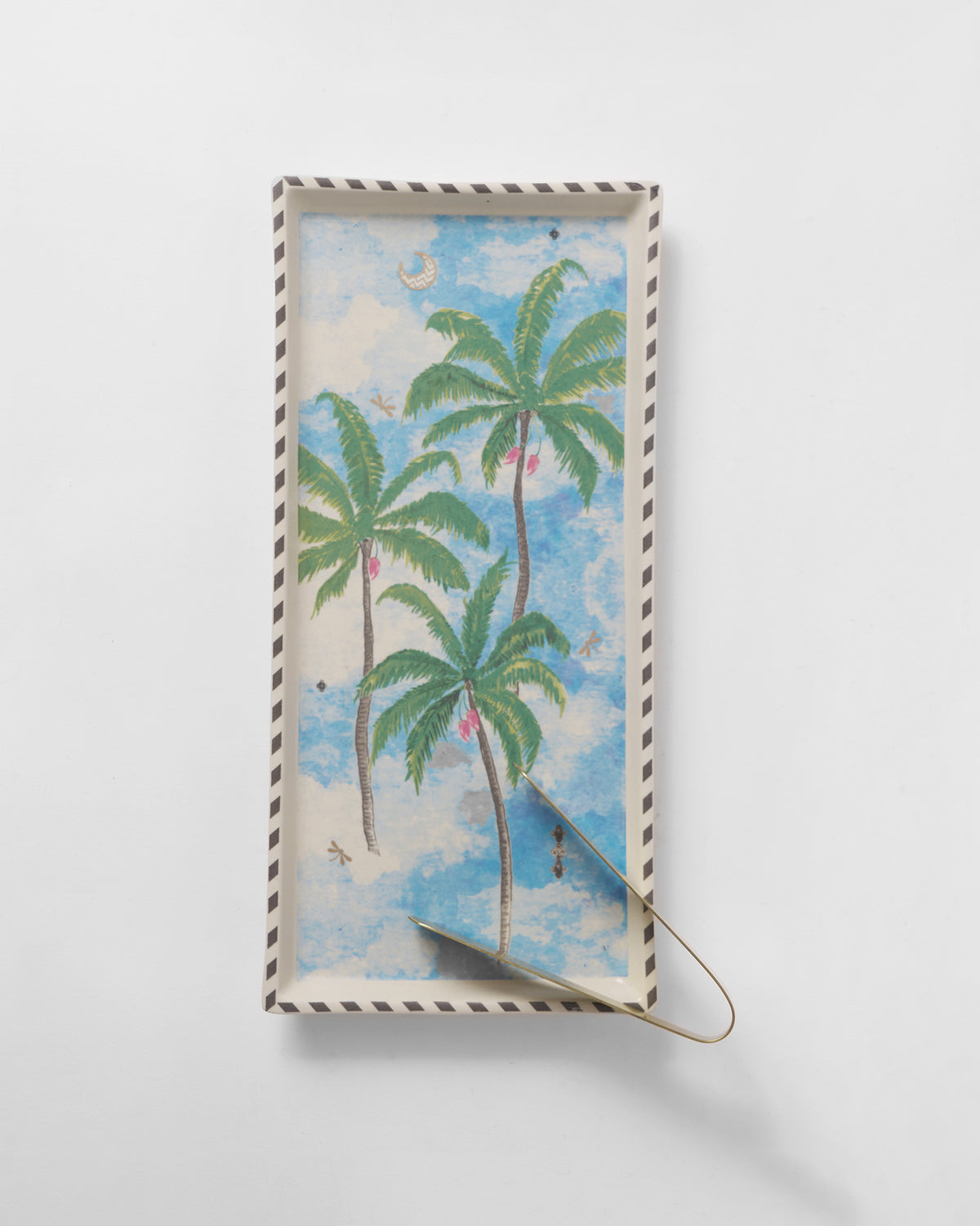 Overhead of a Haathi cookie tray showing palm trees, a striped rim, and gold tongs.