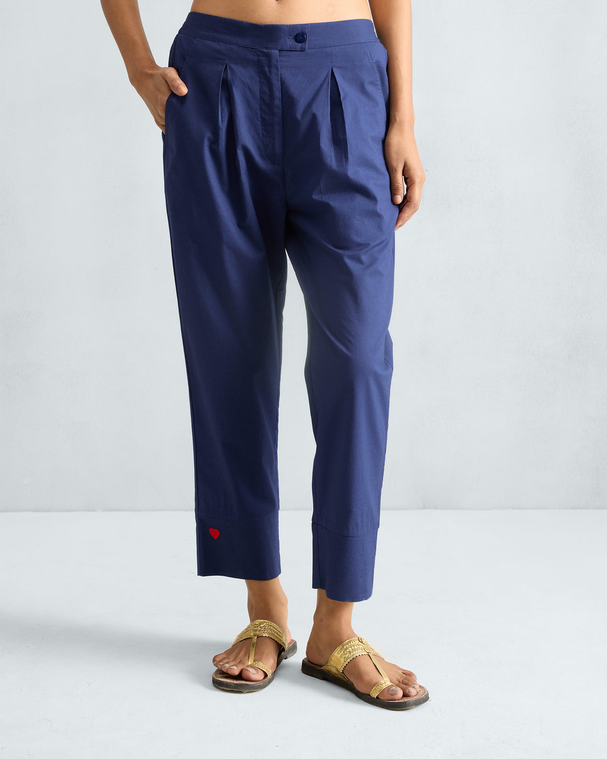 Person wearing ink blue narrow pants with front pleats and a red heart near the hem.