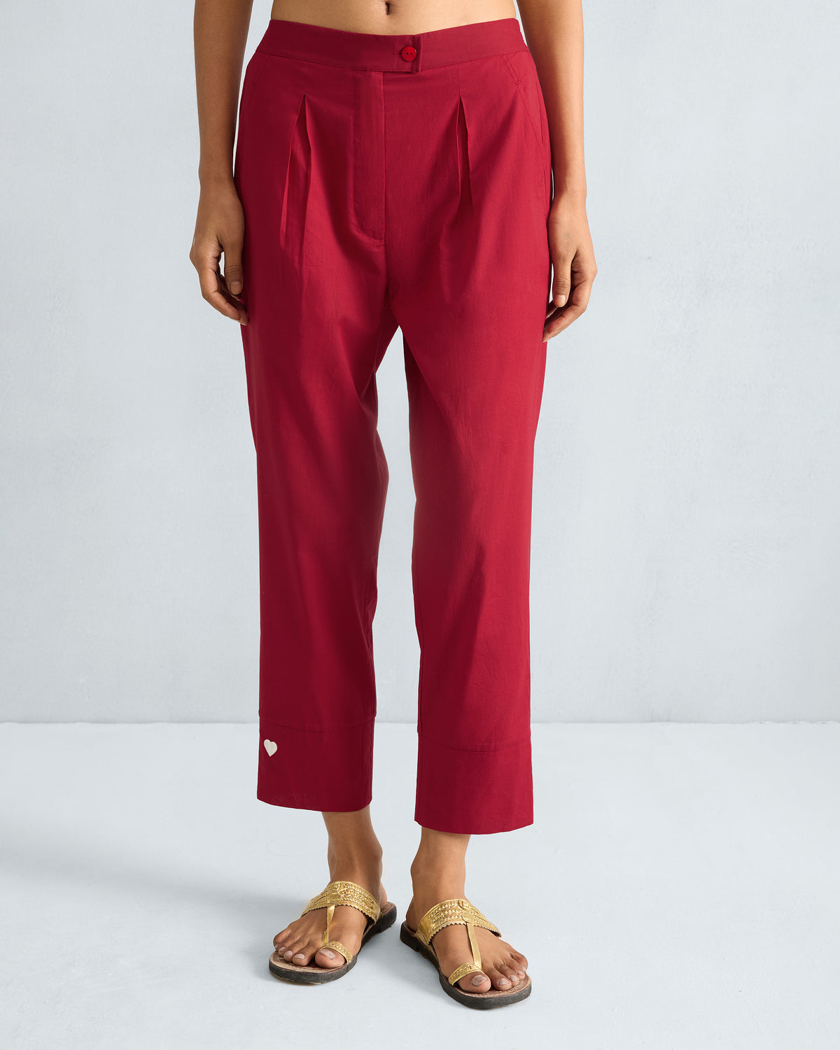 Person wearing red narrow pants with front pleats and a white heart near the hem.