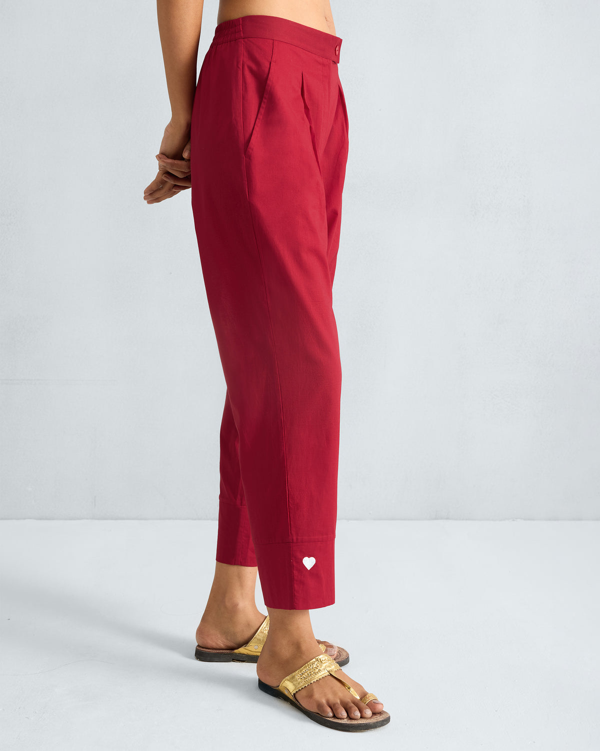 Side view of red narrow pants showing the tapered crop and white heart detail.