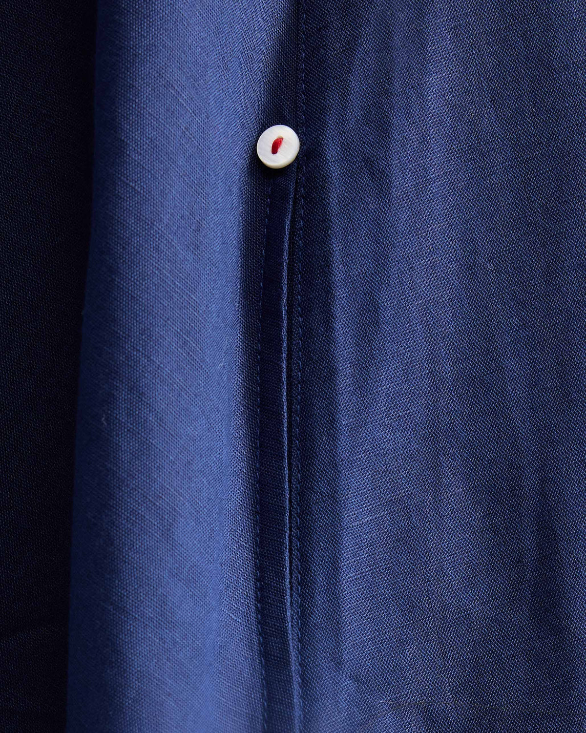 Close-up of an ink blue Double Layer Dress button with red stitching.