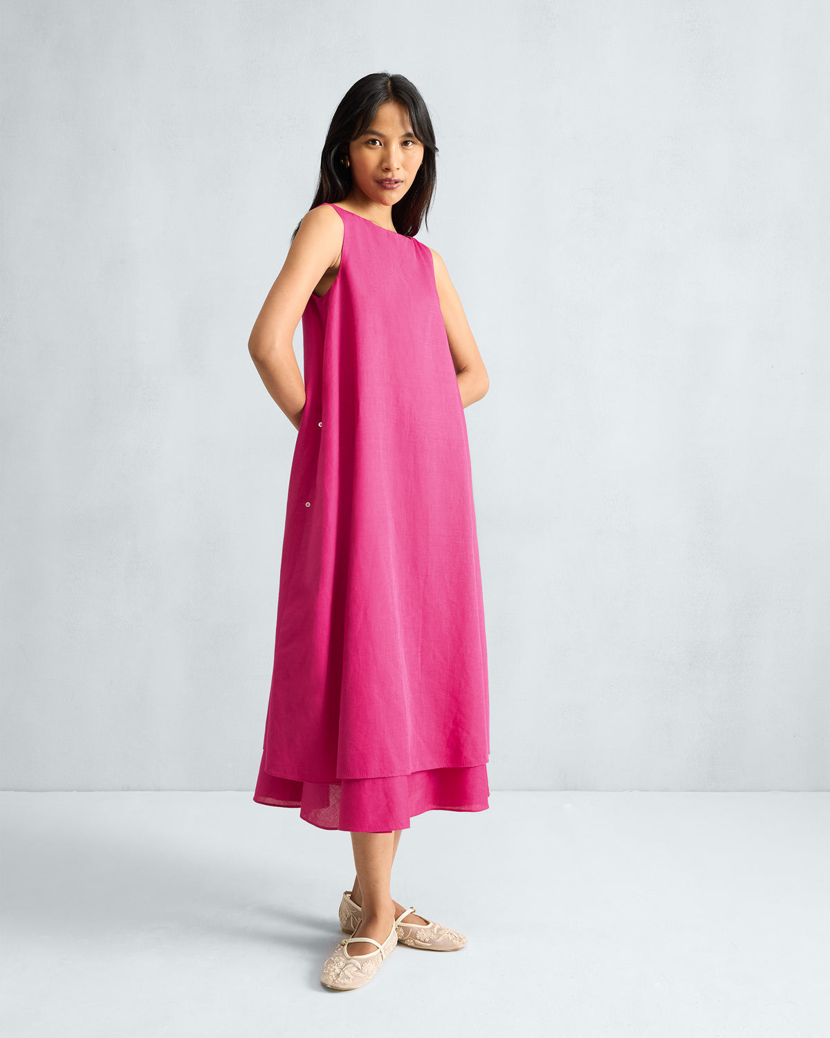 Person wearing a fuchsia sleeveless midi dress with a layered hem.