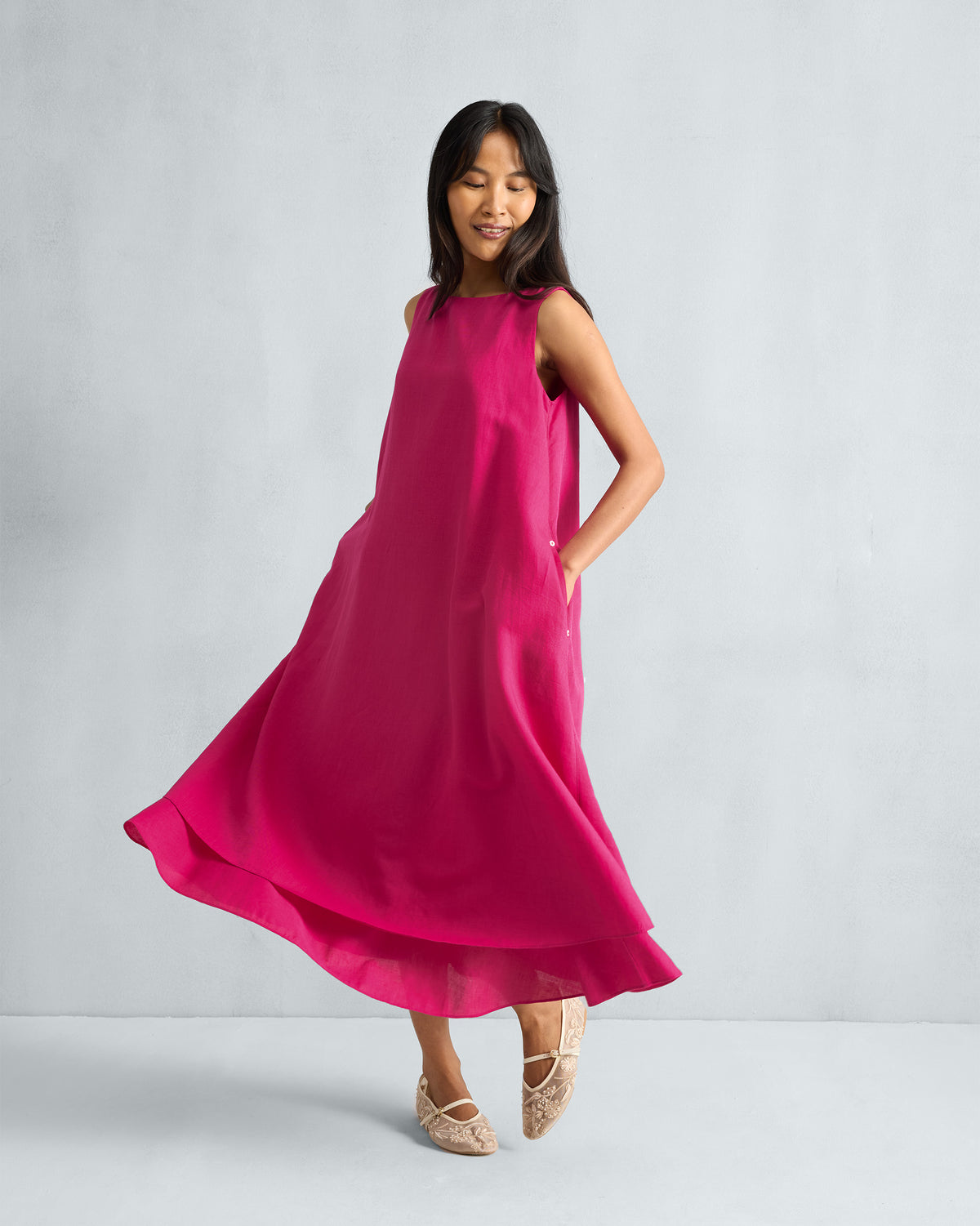 Person wearing a fuchsia sleeveless midi dress with hands in the pockets.