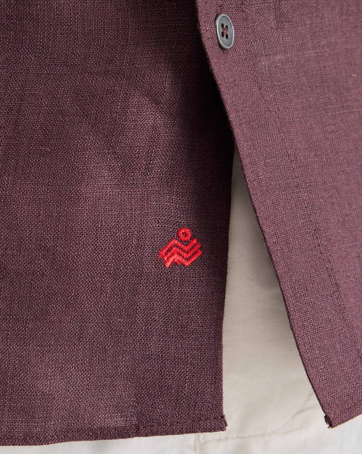 Close-up of red embroidery near the hem of a chocolate plum half-sleeve shirt.