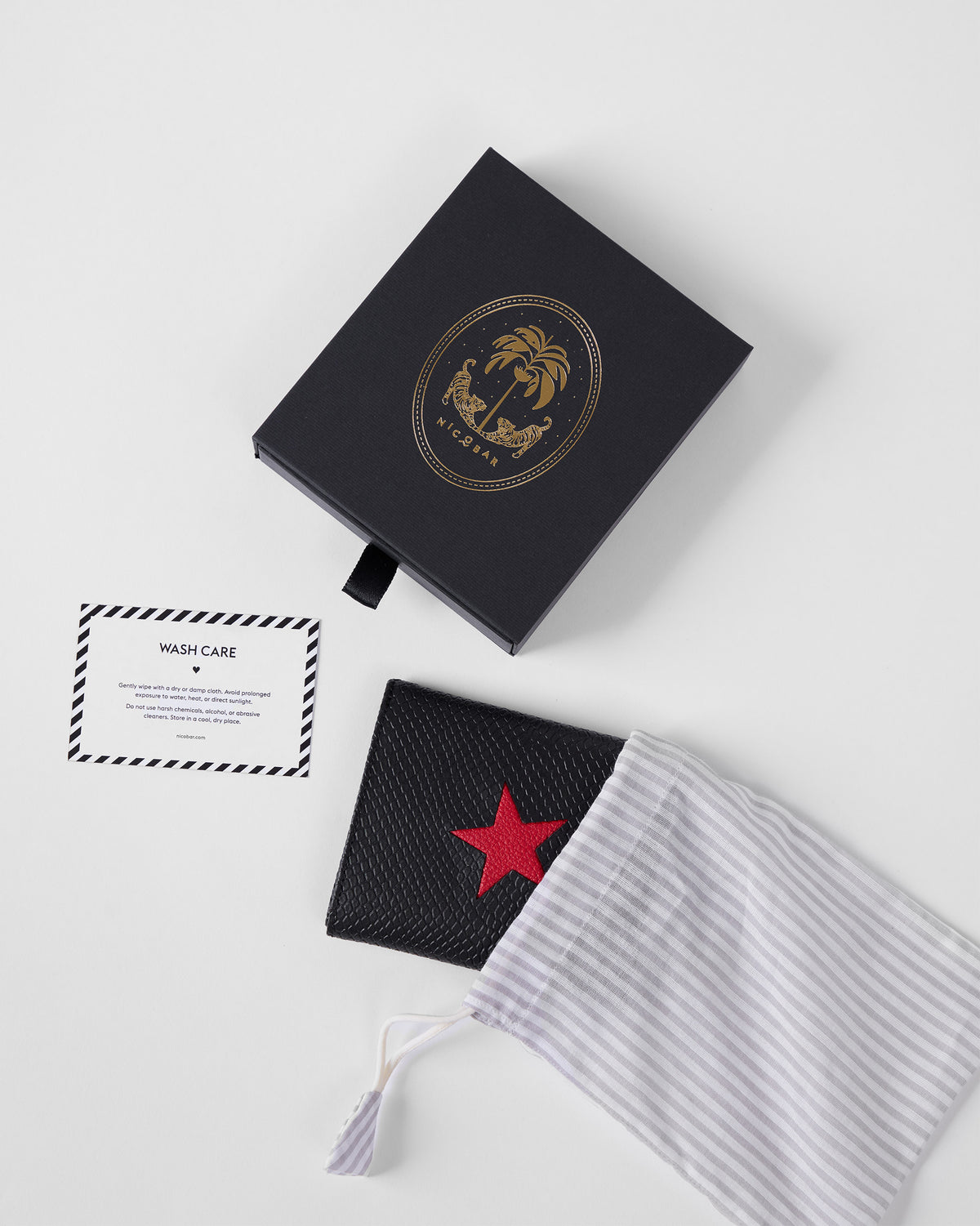Black red-star wallet with striped dust bag and black Nicobar gift box.