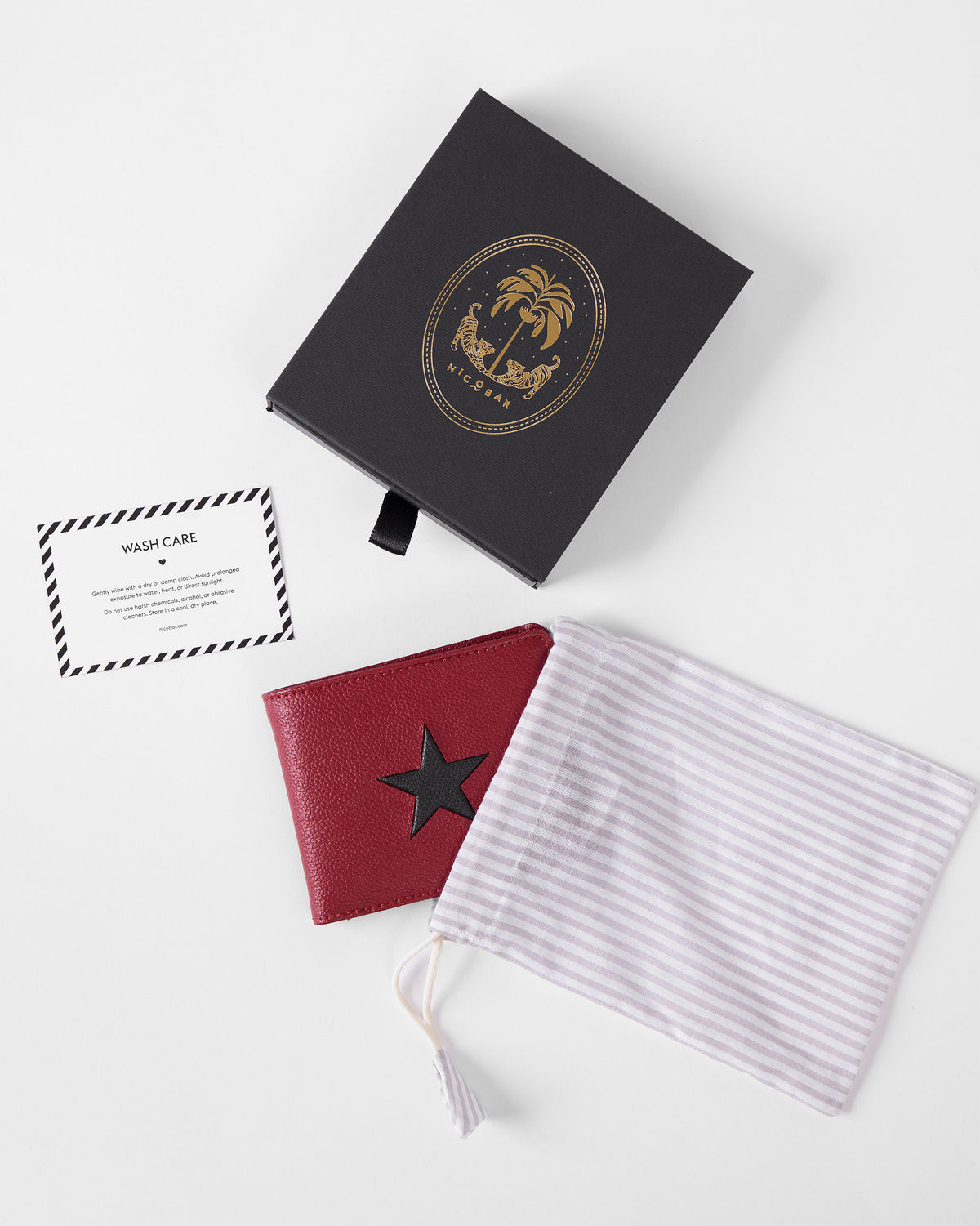 Red star wallet beside a black Nicobar box, striped pouch, and care card.