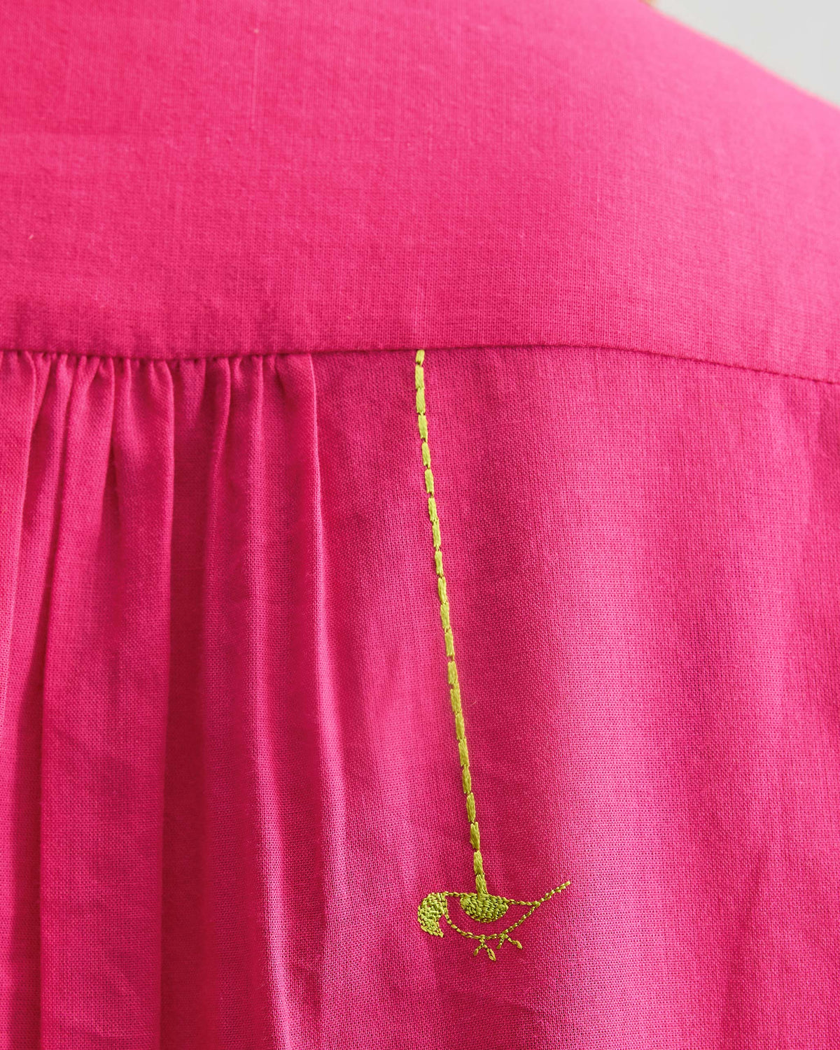 Close-up of a green parrot on a fuchsia mandarin collar top.