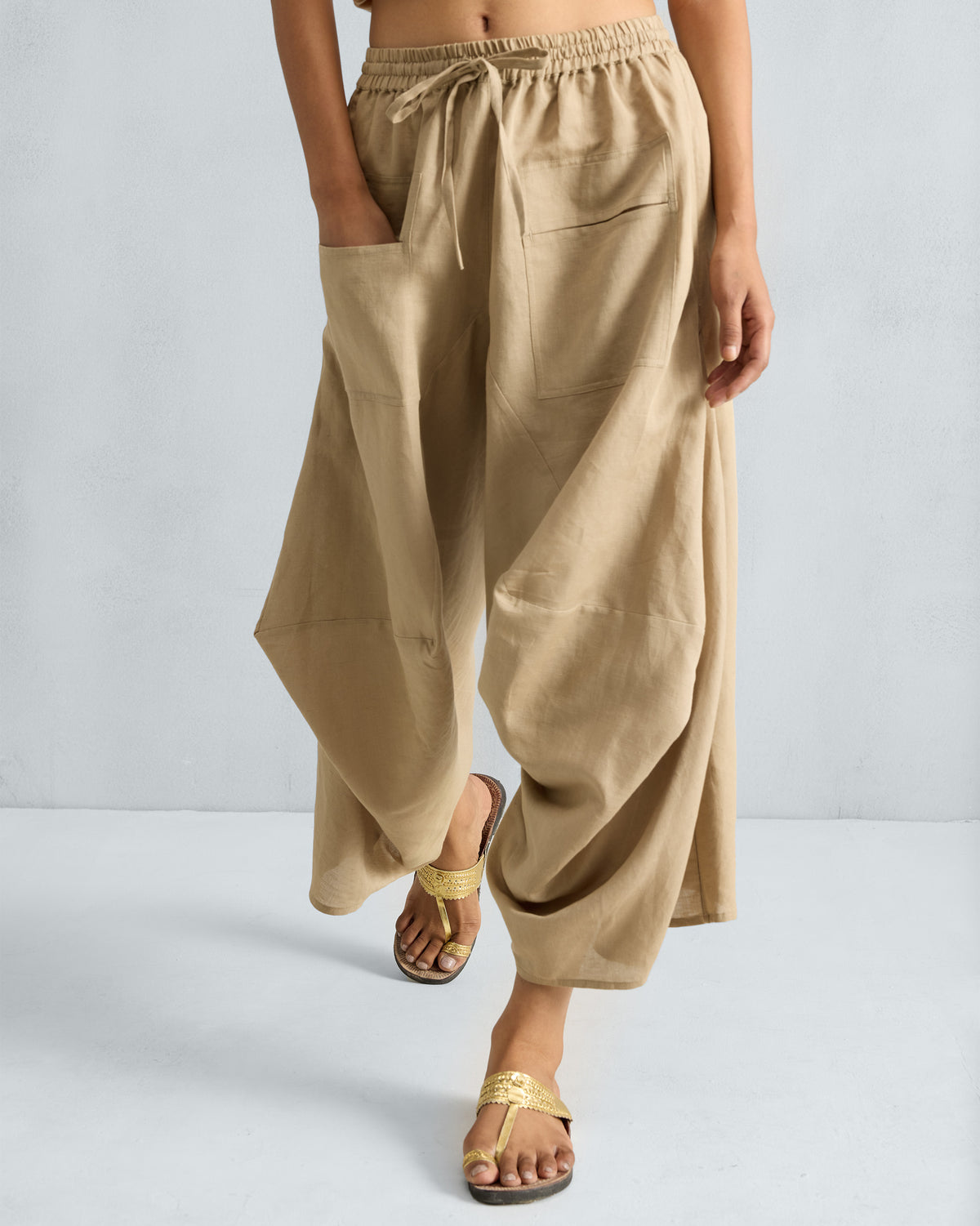 Person wearing beige Yoka Trousers with a drawstring waist and patch pockets.