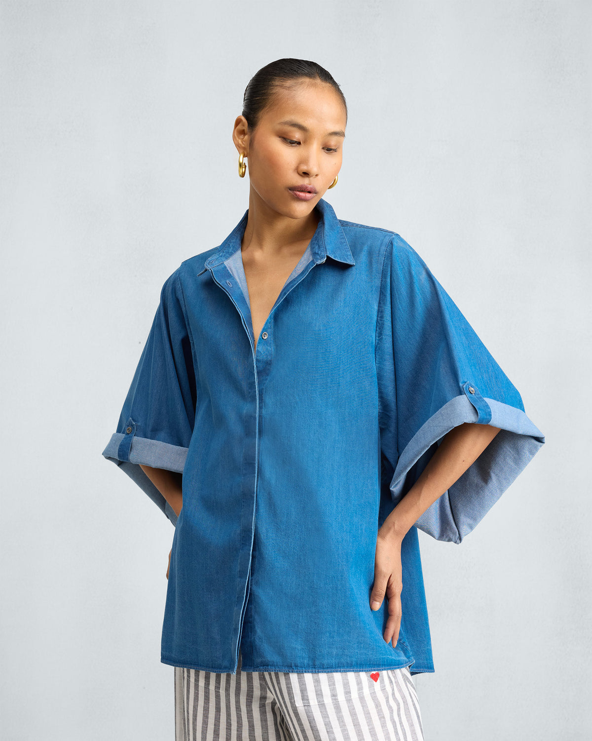 Person wearing a blue denim shirt with wide button-tab sleeves.