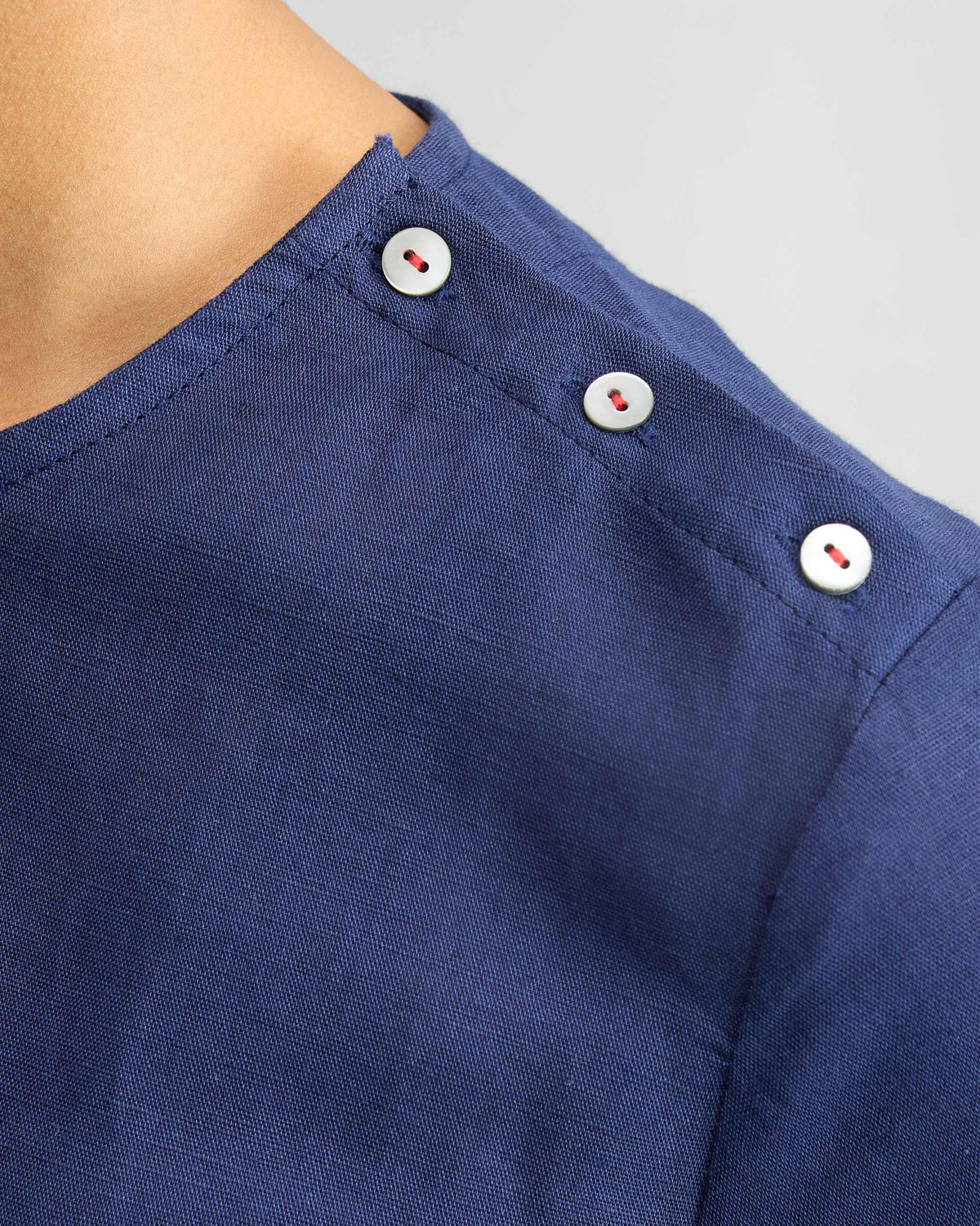 Close-up of red-stitched buttons on the shoulder of an ink blue High Slit Top.