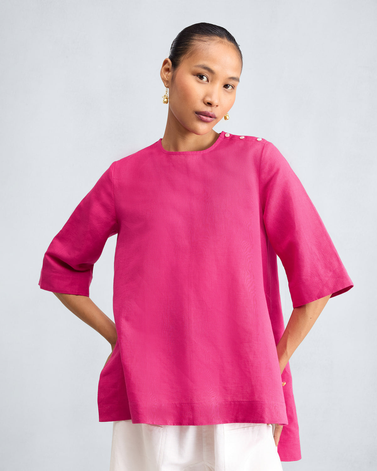 Person wearing a fuchsia top with white buttons on the shoulder.