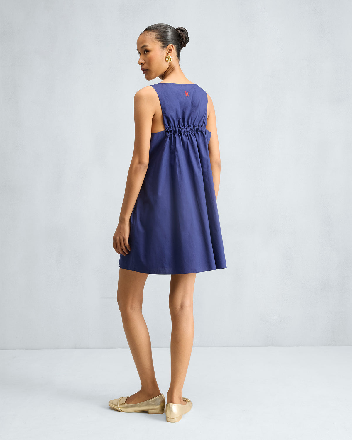 Back of an ink blue short racerback dress with elastic gathering and a red star.