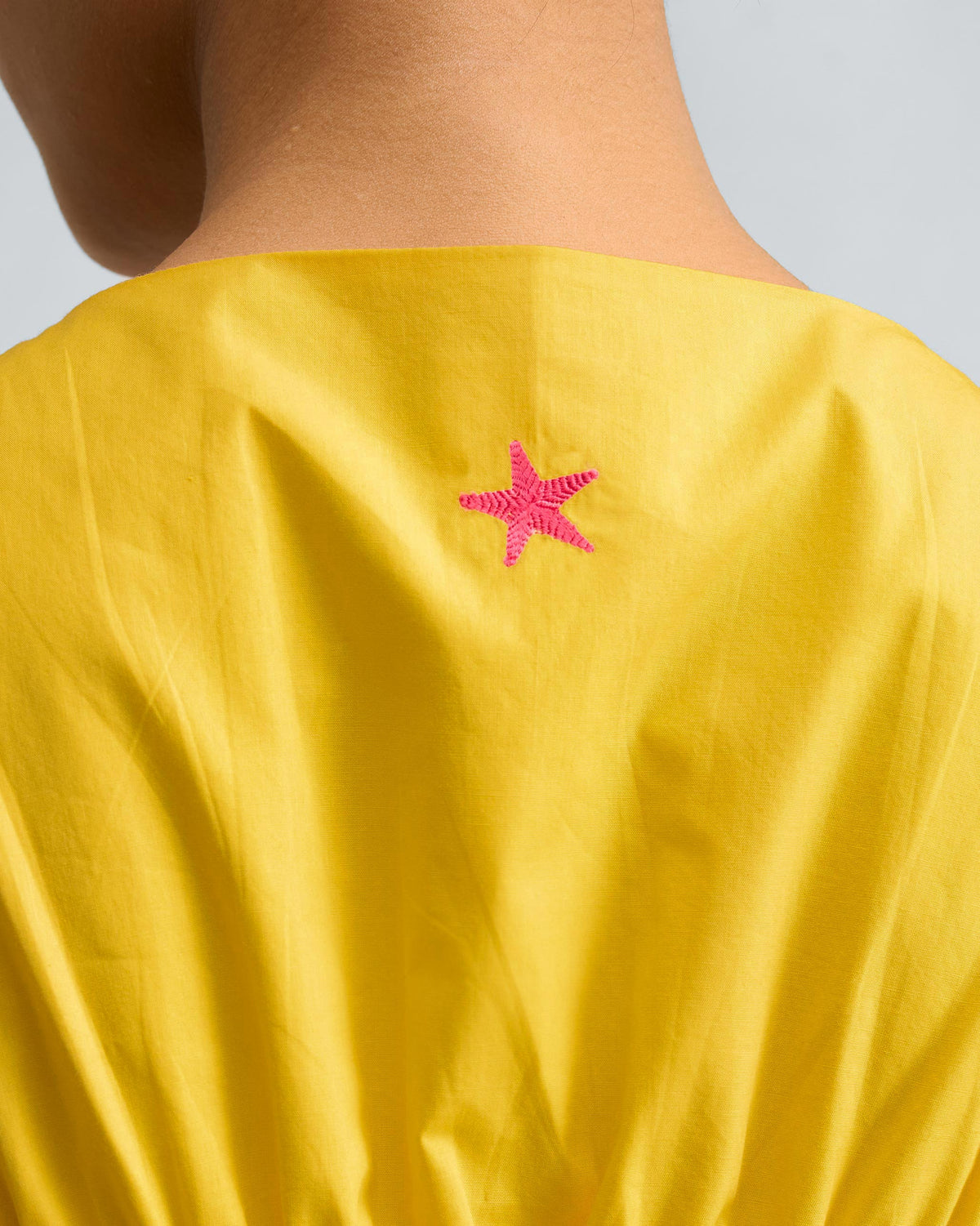 Close-up of a pink star on a yellow short racerback dress.