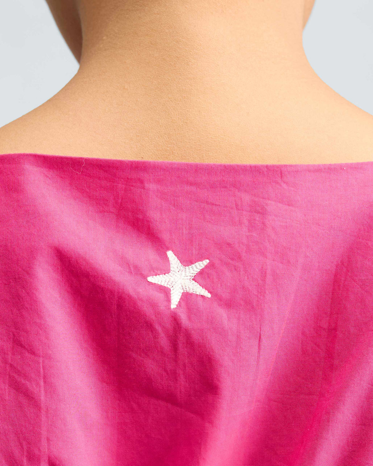 Close-up of a fuchsia short racerback dress with a white star on the back.