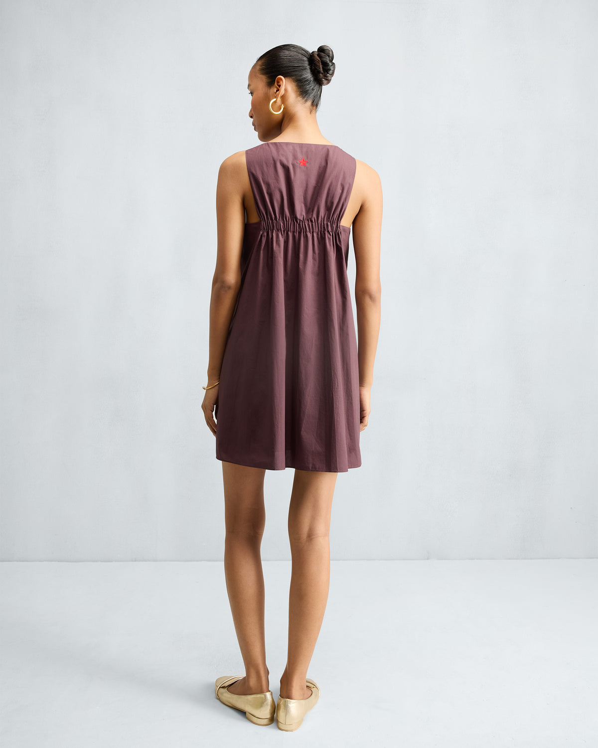 Back of a chocolate plum short racerback dress with elastic gathering and a red star.