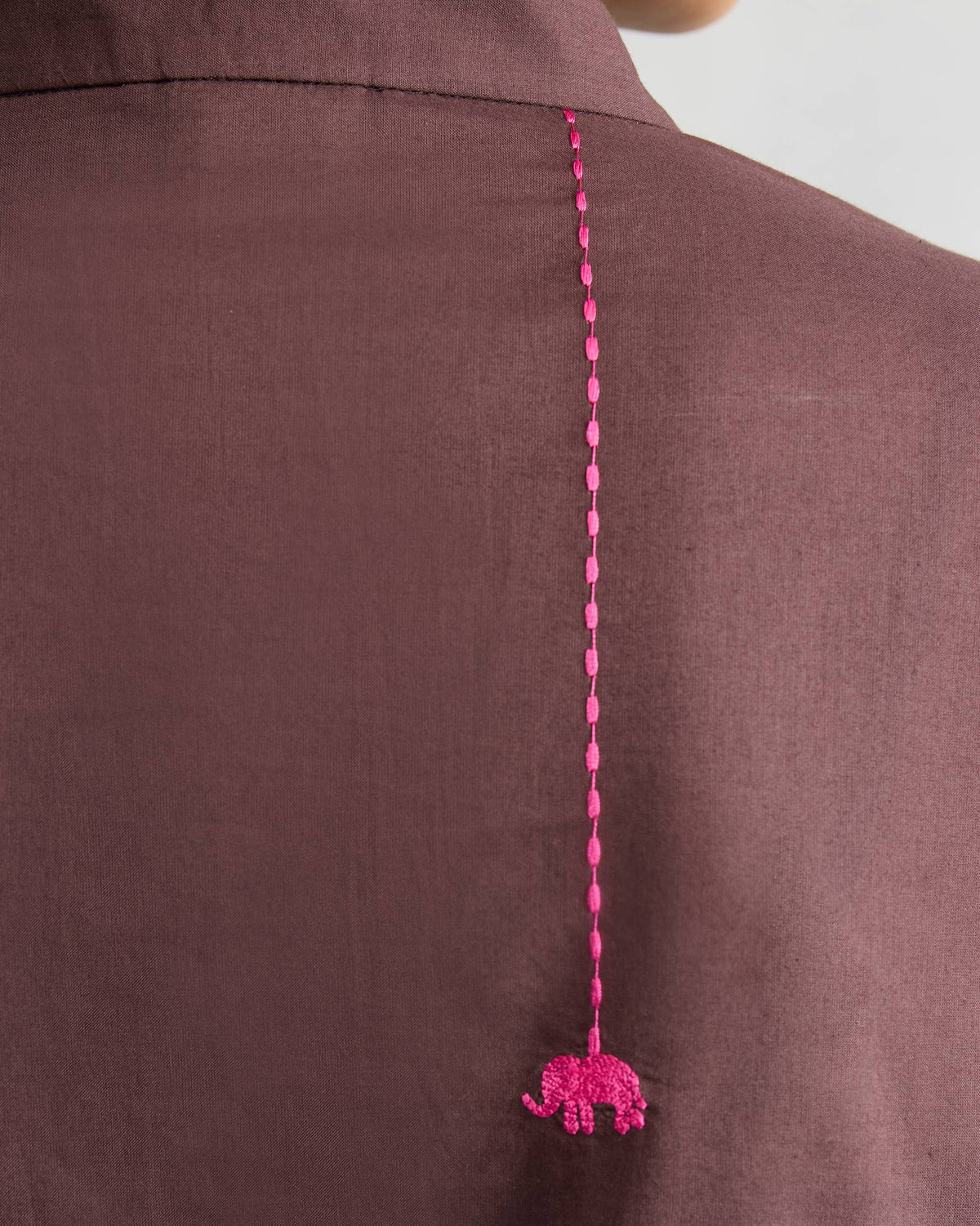 Close-up of a pink embroidered elephant on a chocolate plum kurta.