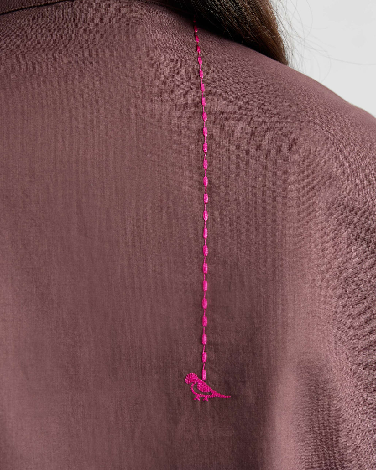 Close-up of a pink embroidered parrot on a chocolate plum kurta.