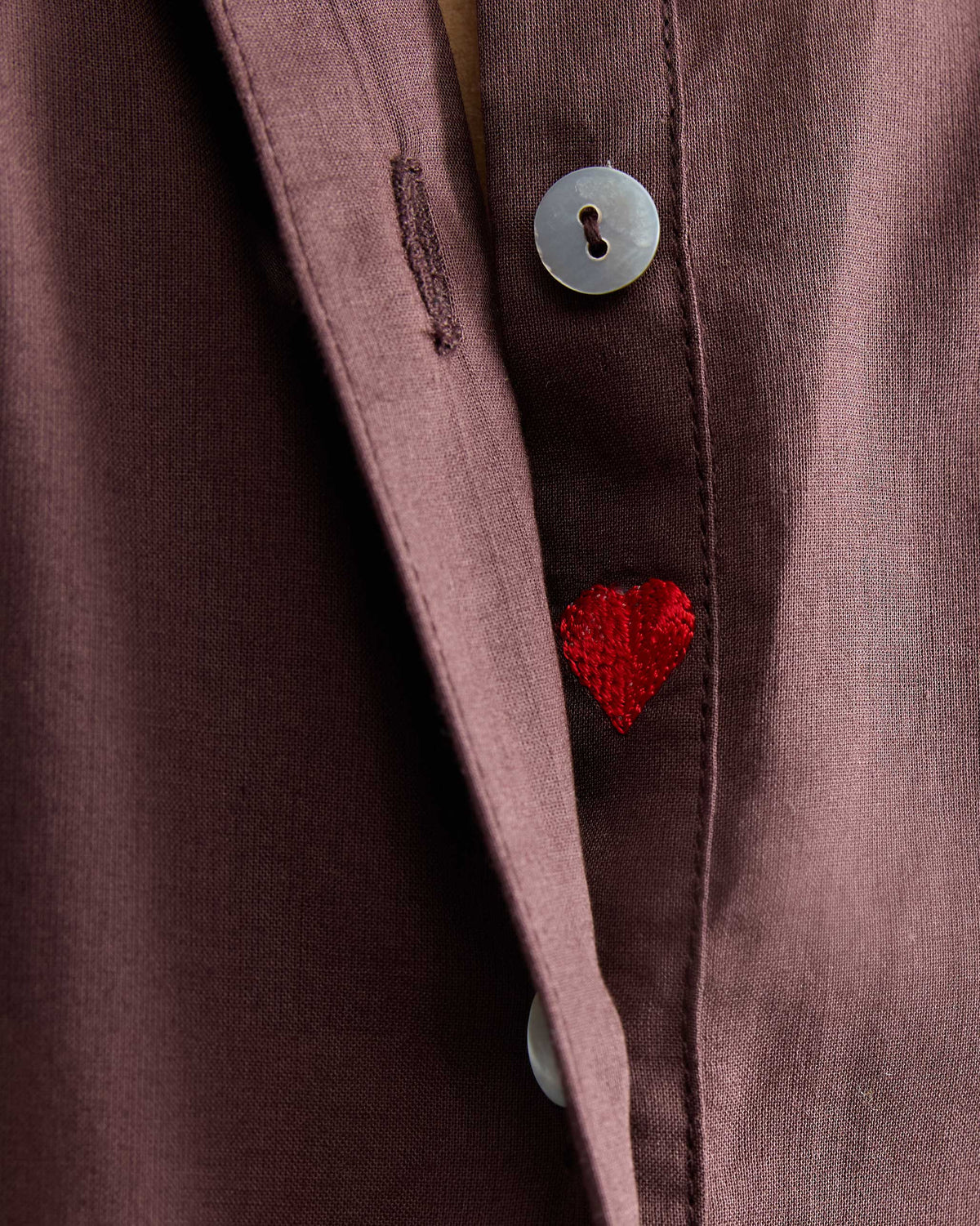 Close-up of a red embroidered heart on the placket of a chocolate plum kurta.