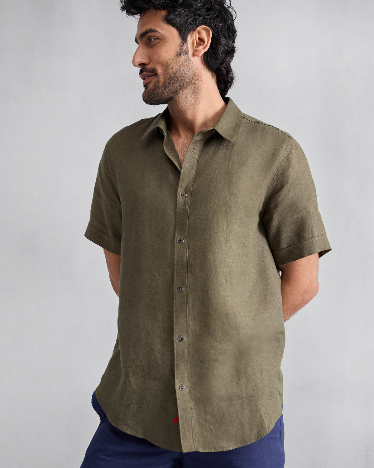 Olive half-sleeve linen shirt worn untucked with a red mark at the placket hem.