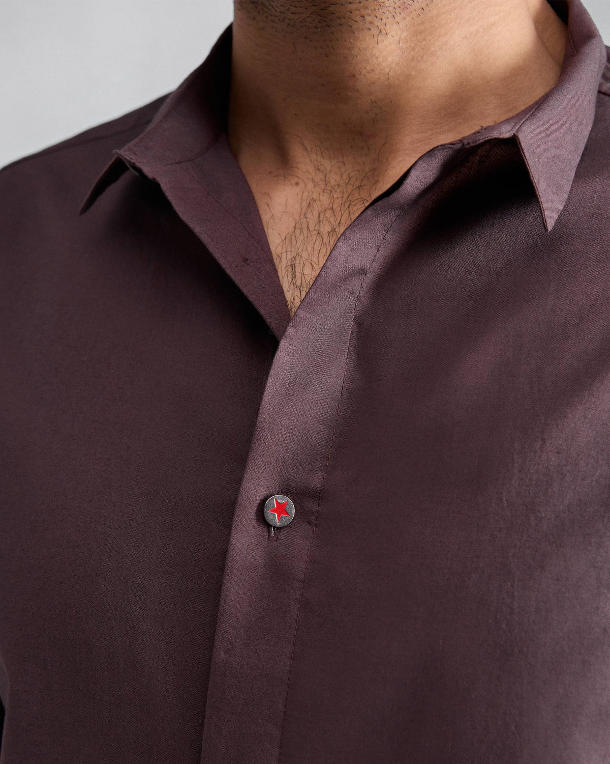 Close-up of a chocolate plum Riverine shirt collar with a red star button.