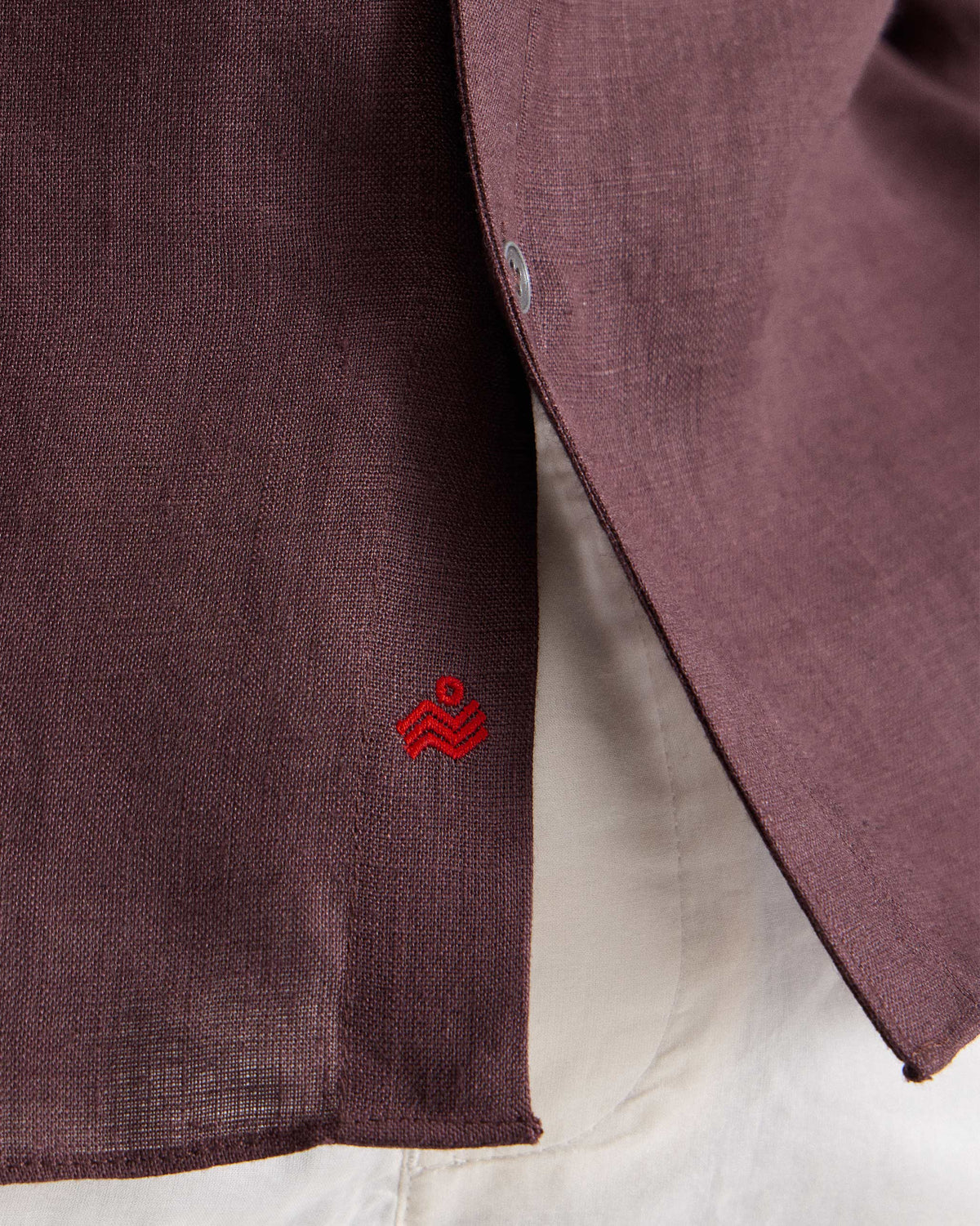 Close-up of a chocolate plum Classic shirt hem with a red Nico logo.