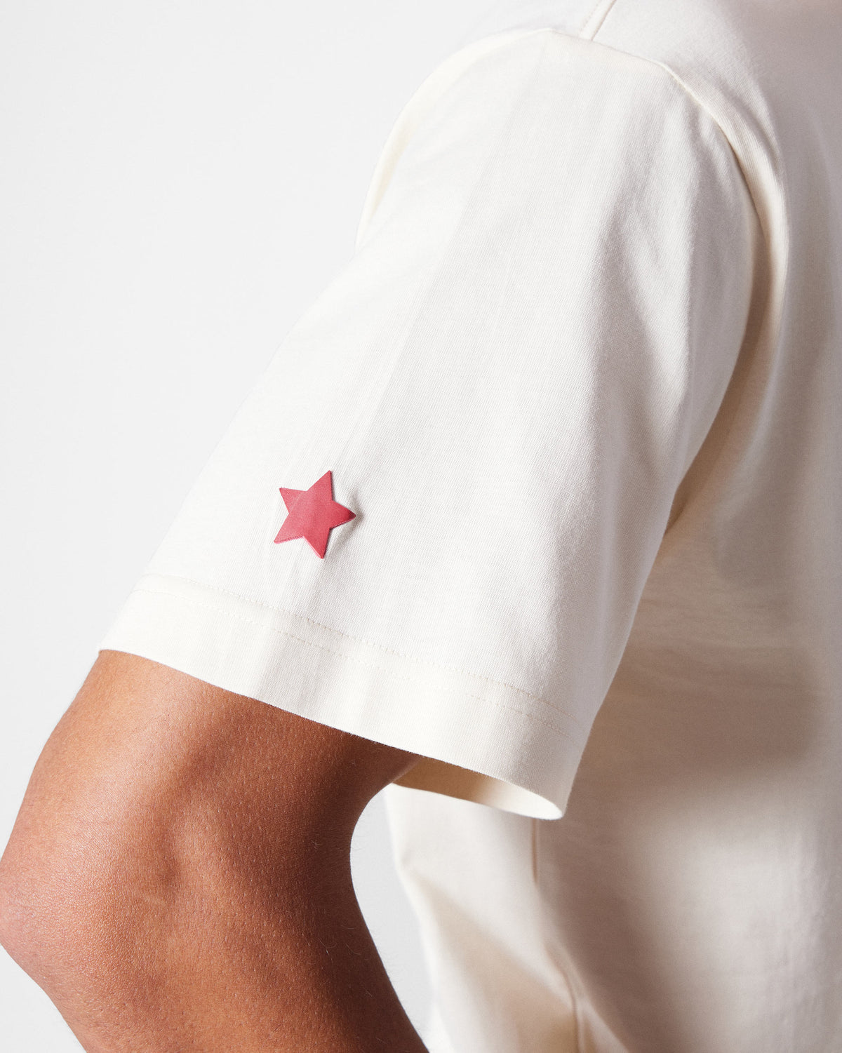 Close-up of a red star on the sleeve of an ivory Bulbul t-shirt.