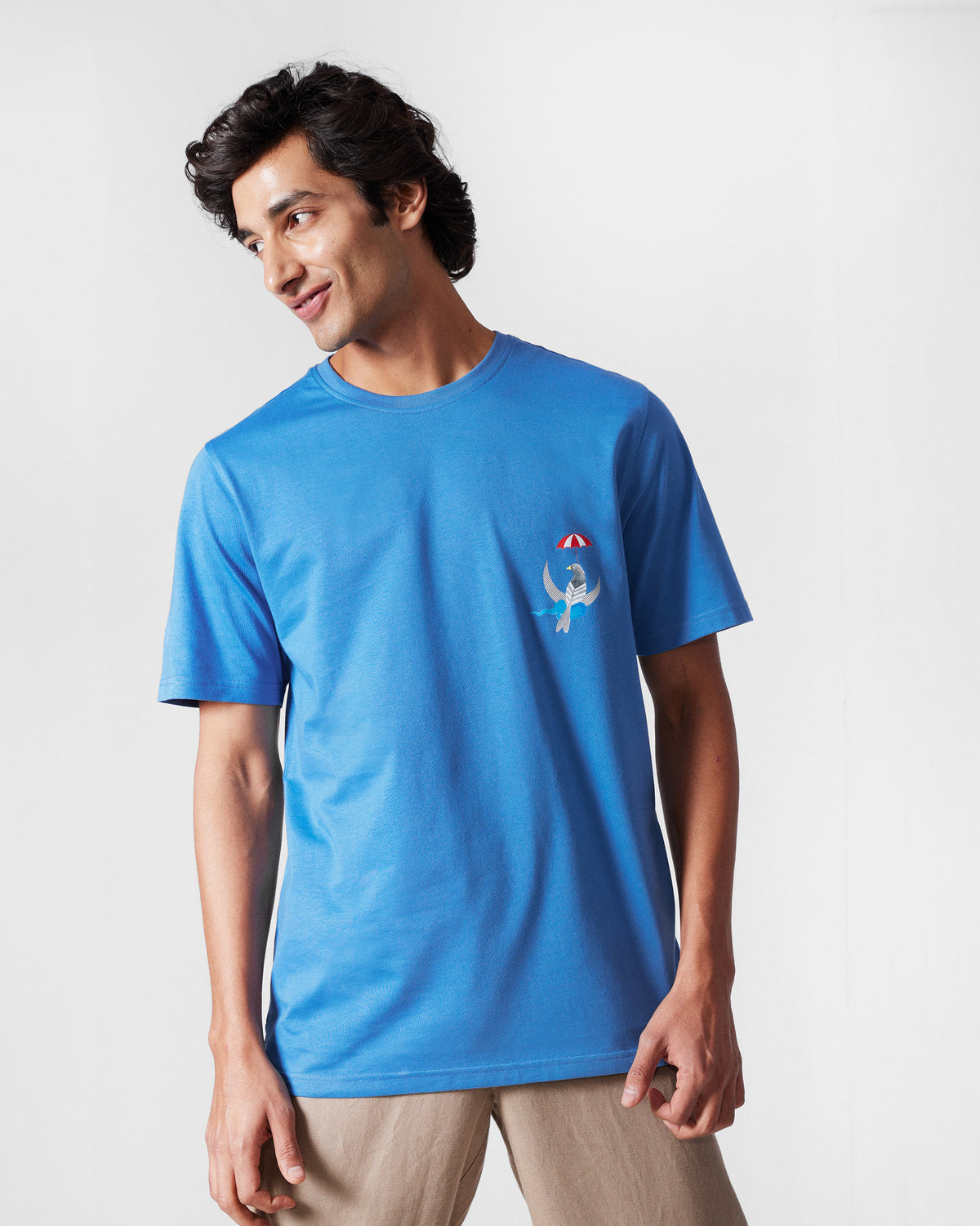 Person wearing a riverside blue Everyday t-shirt with a bird and umbrella chest motif.